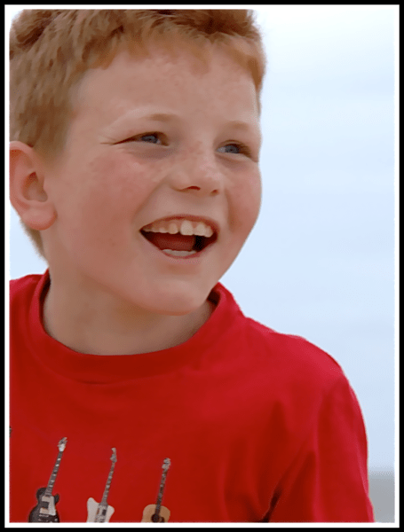 Alfie in colour laughing wearing a red t-shirt with guitars on the front
