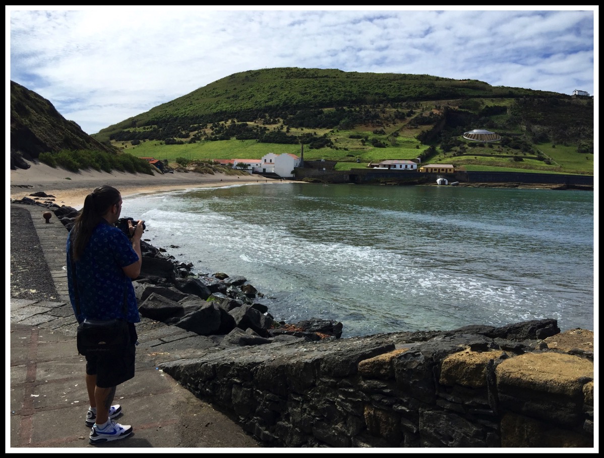 Me stood on the left with volcanic rock beach all around and a view of the bay