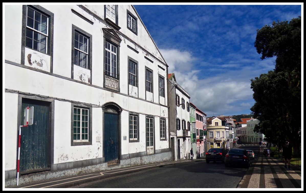 White buildings line the left of the pavement and road filling the whole image