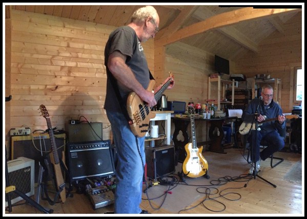 Phil stood playing bass in the centre in front of lots of guitar aps with Sarah's Dad playing guitar on the right hand side of the image