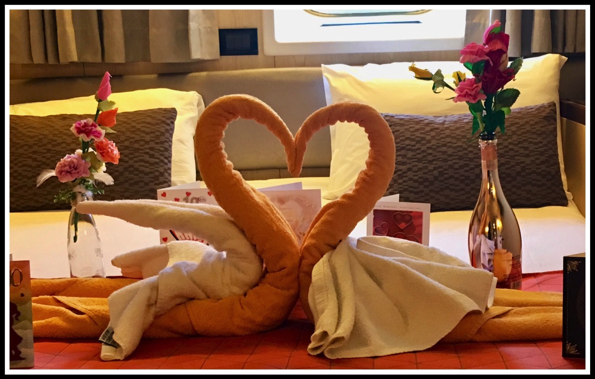 two towel swans together in a love heart shape surrounded by our anniversary cards, on the bed of our cabin on the ship