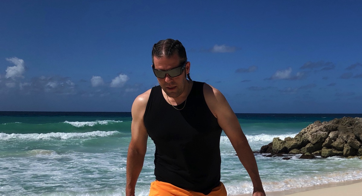 Me wearing a black best and orane shorts waling along the beach in Barbados with braided hair too