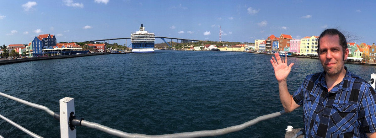 Me stood on the right of a panorama with the boat in the centre and the colourful buildings behind me.