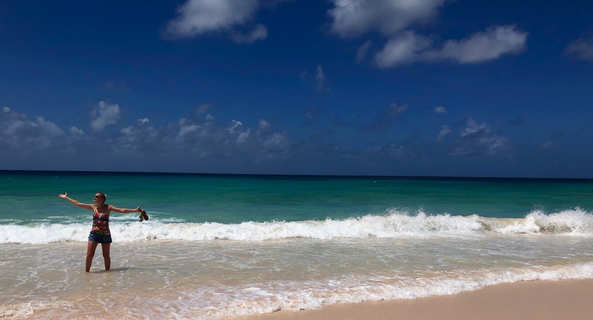Sarah with arms in the air on the far left of the photo, running along an empty beach in Barbados