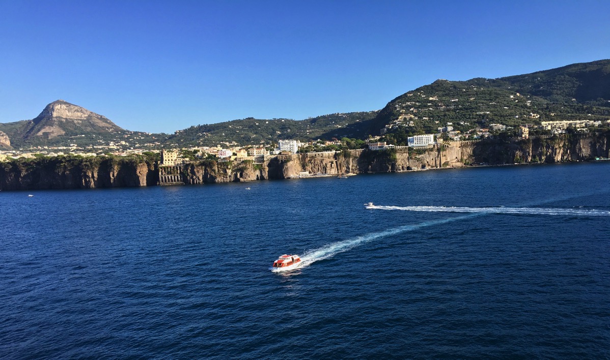 A little boat zig zagging across the sea with the town in the background
