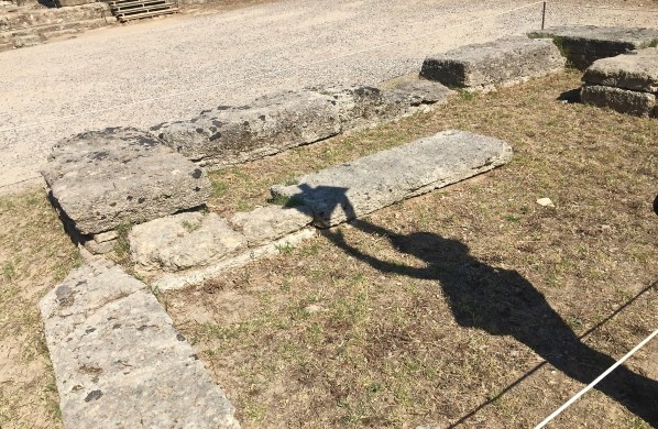 A shadow across the sandy floor of our guide pretending to light the torch from the ancient games at the exact spot