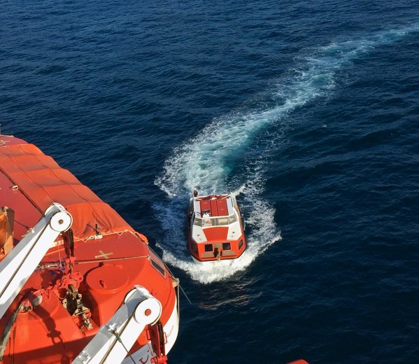 Close up of the little boat now pulled up alongside the ship whilst leaving lots of frothy waves behind