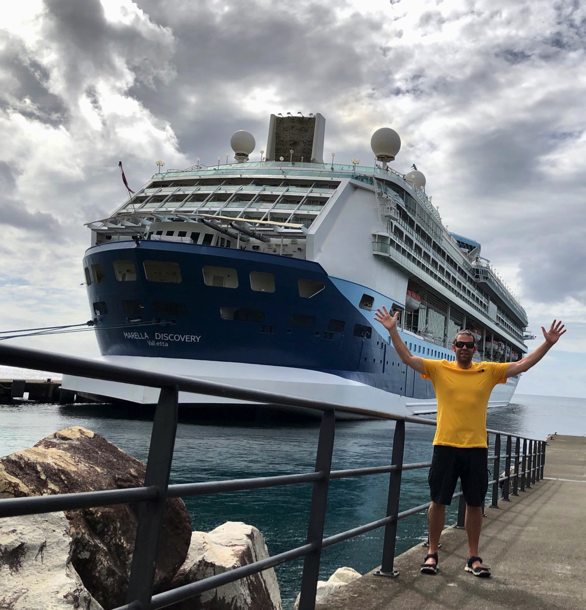 Me in a bright yellow t-shirt waving my arms in the air in front of the cruise ship