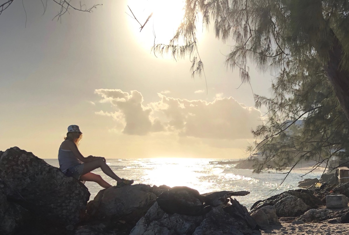 Sarah sat on rock in front of a beautiful Barbados sunset