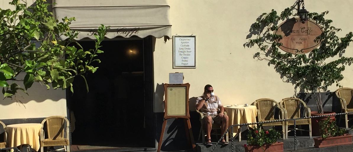 Me sat in the sun outside the cafe eating a coissant and drinking an espresso ith the road right in front of me