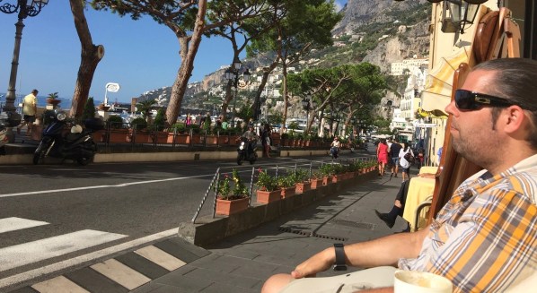 Me sat in the sun outside the cafe eating a coissant and drinking an espresso ith the road right in front of me
