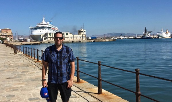 me stood on the dock carrying the blue sicily baseball cap i'd just bought with the seascape of boats behind me