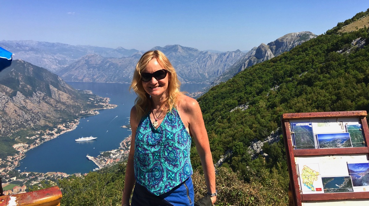 Photo of Sarah stood in front of and incredible landscape of mountains and a valley looking right down to our ship in the sea a t the bottom