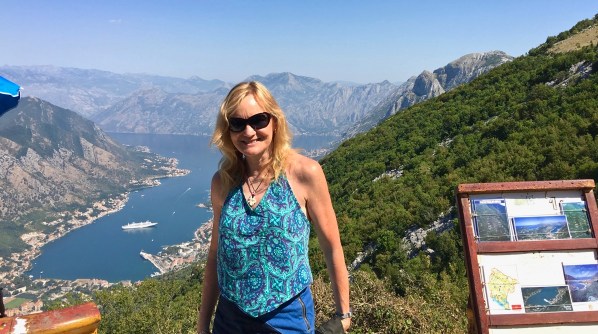 Photo of Sarah stood in front of and incredible landscape of mountains and a valley looking right down to our ship in the sea a t the bottom