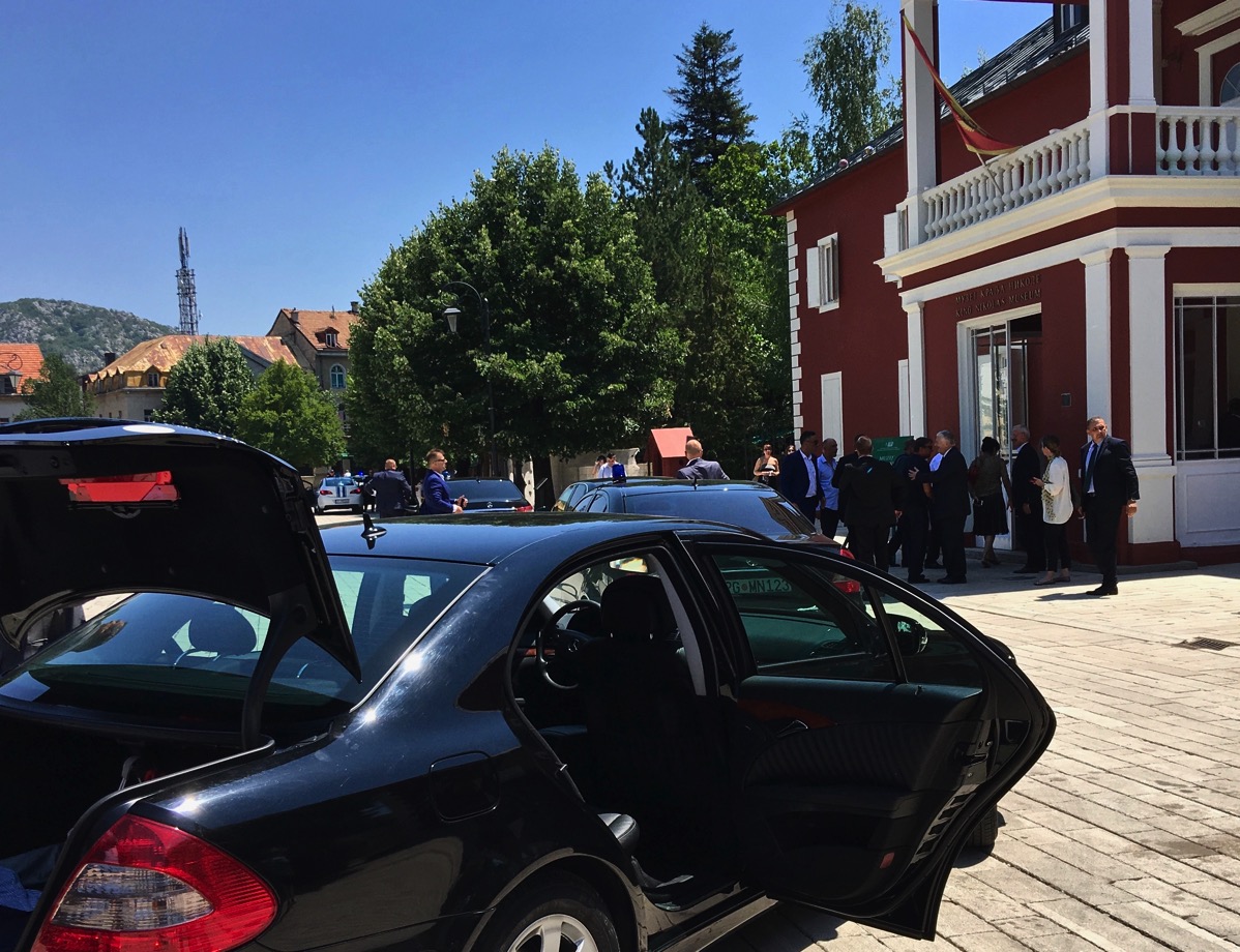 Photo taken behind a secret black police car with the door open and in front is the president of Montenegro