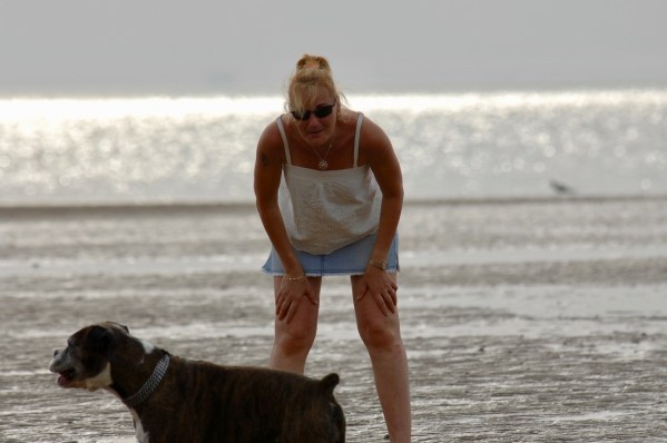 Sarah bent and resting her hands on her knees exhausted after a run with Bruce (bottom left) on hunstanton beach with the sea in the background