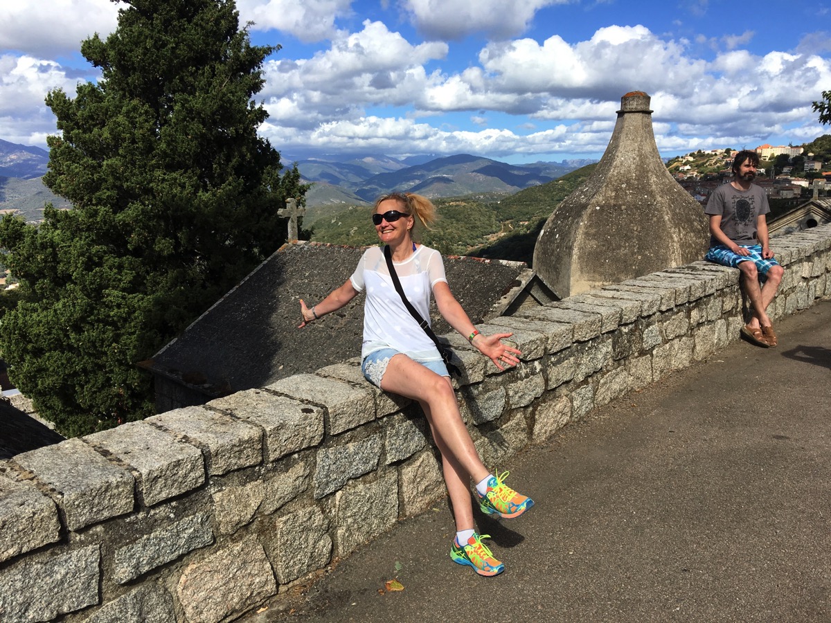 Sarah sat against a wall with the hills of Corsica behind her