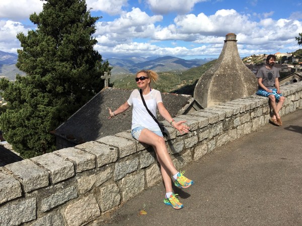 Sarah sat against a wall with the hills of Corsica behind her