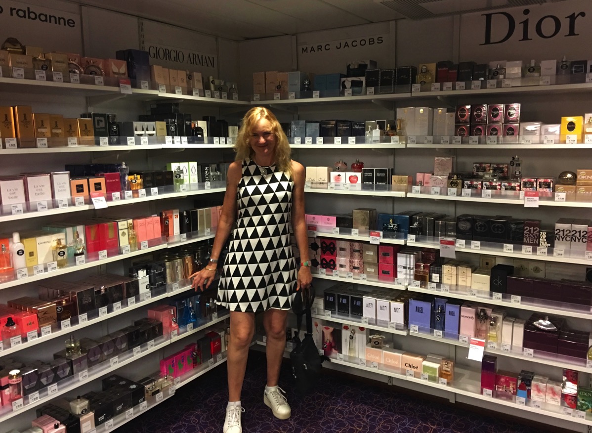 Sarah in a black and white dress stood in front of lots of hand bags in the ship shop