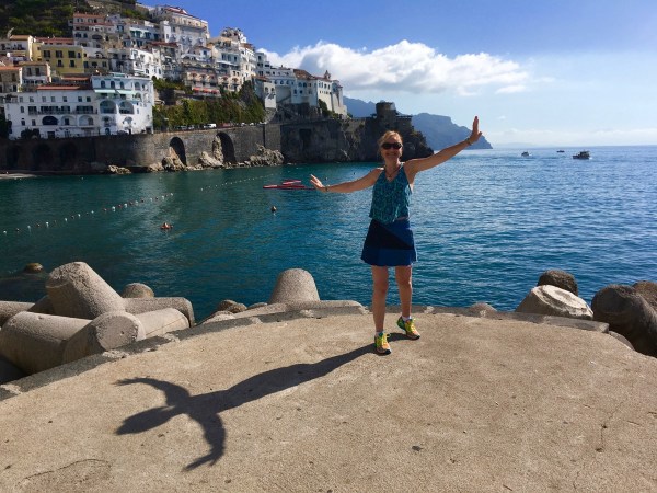Sarah stood on the edge of the small dock with sea all around her and mountains in the background.jpg whilst showing her guns again in the bicepts pose