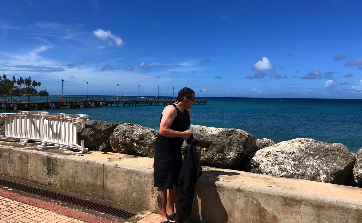 me stood unwrapping the coconut slice in front of the sea and a wall