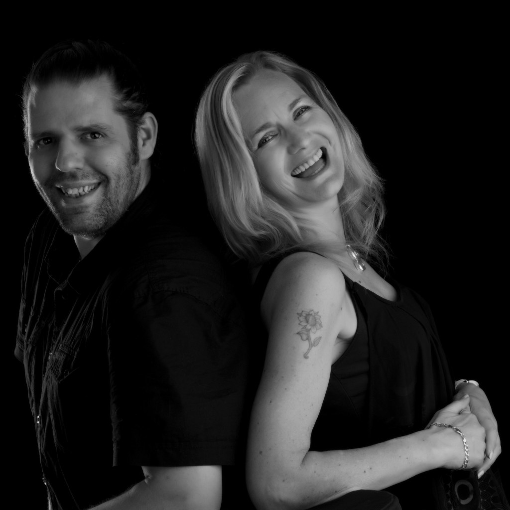 A couple smiling joyfully while standing back to back, showcasing their love and happiness in a black and white photograph.