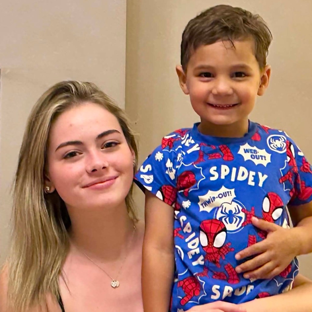 Ella on the left, a young woman with straight blonde hair wearing a fine pendant necklace, smiling gently at the camera. On the right, a young boy known as Mighty Mike, grinning happily while wearing a bright blue Spider-Man t-shirt covered in cartoon superhero graphics.